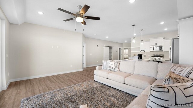 living room featuring wood-type flooring, a barn door, sink, and ceiling fan