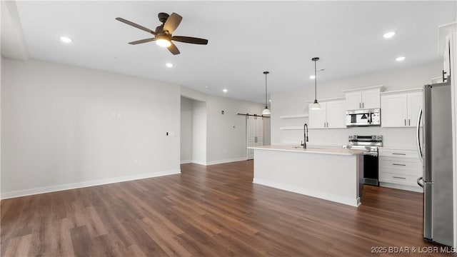 kitchen featuring white cabinetry, hanging light fixtures, a center island with sink, appliances with stainless steel finishes, and a barn door