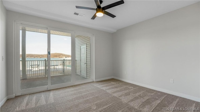 carpeted empty room featuring a water view and ceiling fan