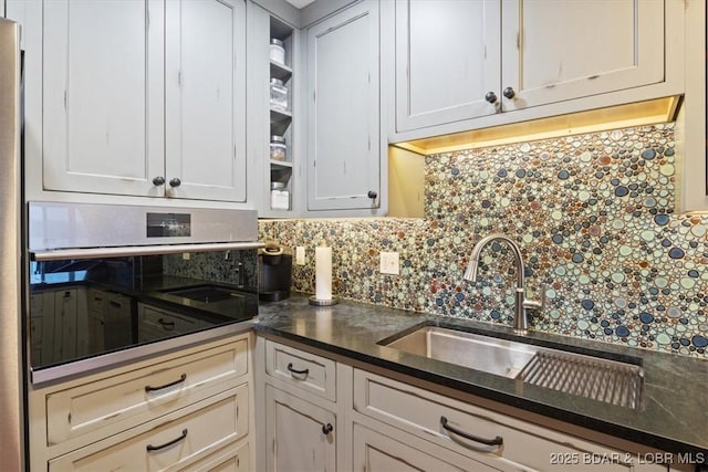 kitchen with sink, tasteful backsplash, dark stone counters, oven, and white cabinets