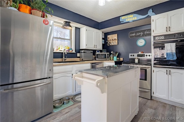 kitchen with appliances with stainless steel finishes, sink, white cabinets, and light hardwood / wood-style flooring