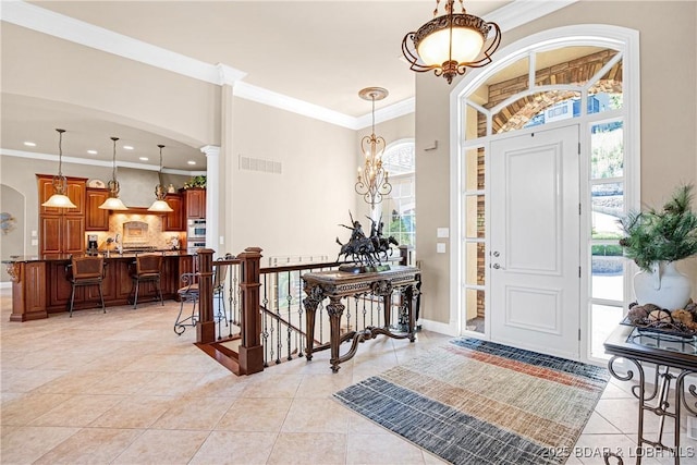 foyer with light tile patterned flooring, crown molding, and a notable chandelier