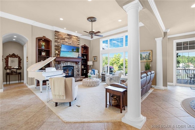 tiled living room featuring built in shelves, a stone fireplace, ornate columns, ornamental molding, and ceiling fan