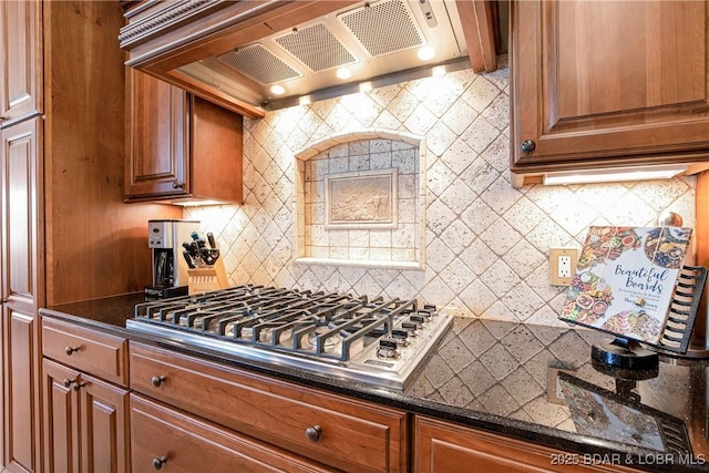 kitchen featuring backsplash, stainless steel gas cooktop, dark stone counters, and premium range hood