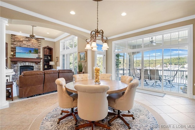 dining area featuring crown molding, ceiling fan, a stone fireplace, and light tile patterned floors