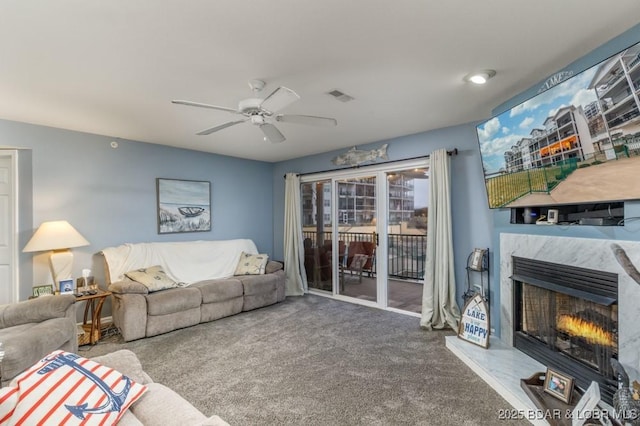 carpeted living room with a high end fireplace and ceiling fan