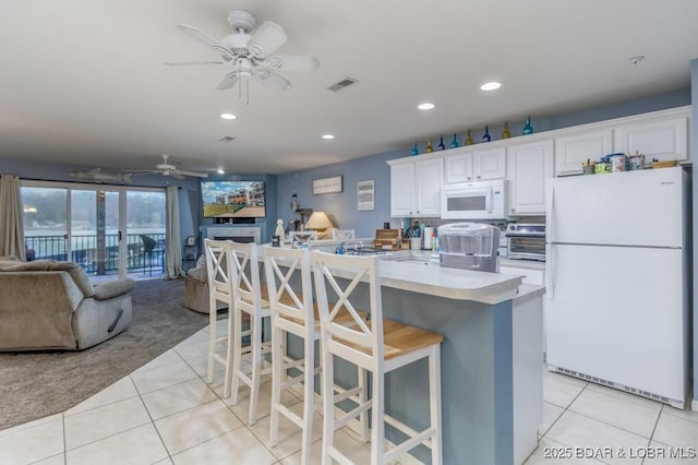 kitchen featuring white appliances, a center island with sink, a kitchen breakfast bar, white cabinets, and light tile patterned flooring