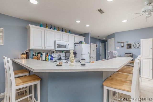 kitchen with a breakfast bar area, backsplash, white cabinets, kitchen peninsula, and white appliances