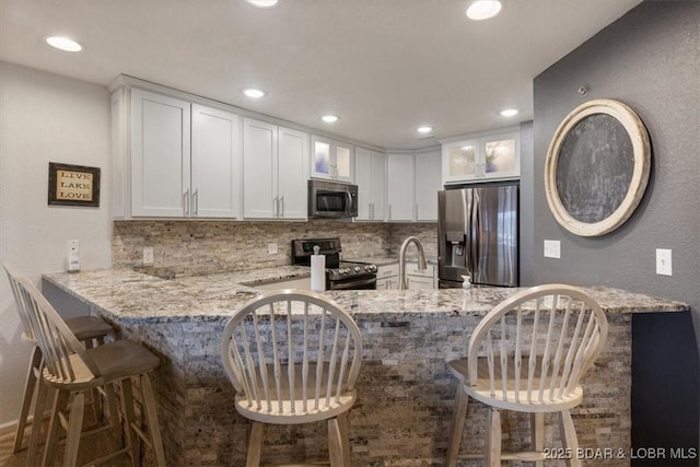 kitchen with light stone counters, a breakfast bar area, white cabinets, and appliances with stainless steel finishes