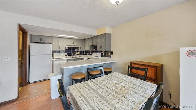 kitchen with gray cabinets, sink, decorative backsplash, kitchen peninsula, and white appliances