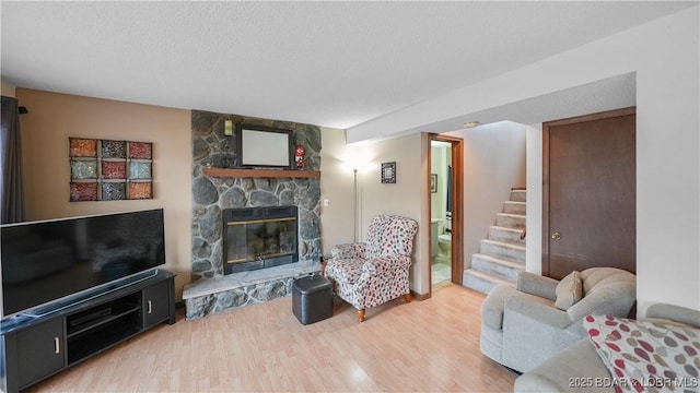 living room featuring hardwood / wood-style floors, a stone fireplace, and a textured ceiling