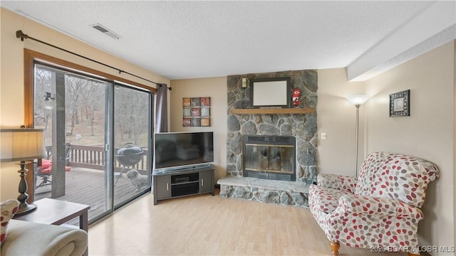 living room featuring wood-type flooring, a stone fireplace, and a textured ceiling