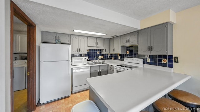 kitchen featuring sink, white appliances, a breakfast bar area, washer / clothes dryer, and kitchen peninsula