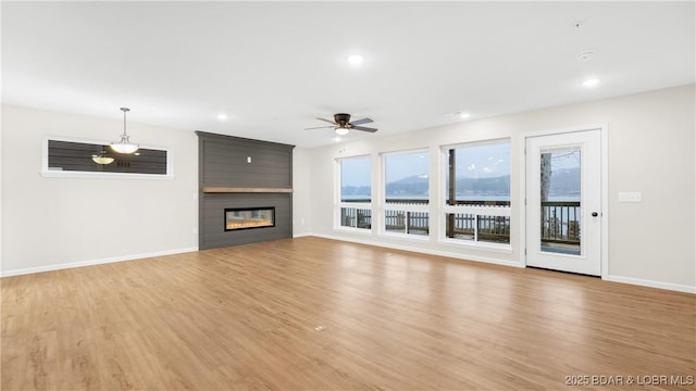 unfurnished living room with wood-type flooring, a large fireplace, and ceiling fan