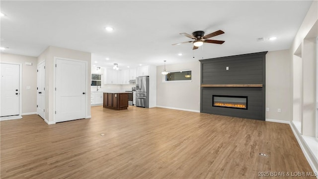 unfurnished living room featuring ceiling fan, a large fireplace, and light hardwood / wood-style floors