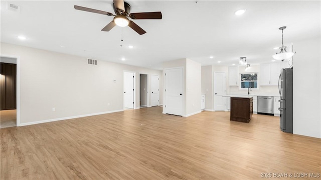 unfurnished living room featuring ceiling fan, sink, and light wood-type flooring