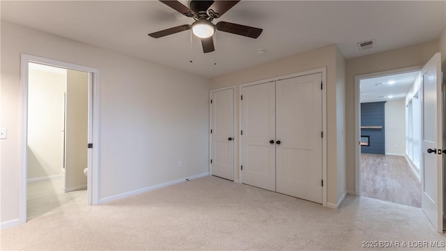 unfurnished bedroom with connected bathroom, a large fireplace, light colored carpet, ceiling fan, and a closet