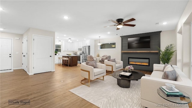 living room featuring ceiling fan, a fireplace, and light hardwood / wood-style flooring