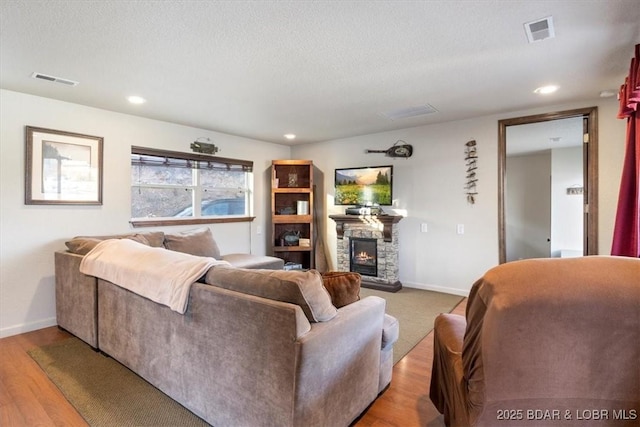 living room with a stone fireplace, light hardwood / wood-style flooring, and a textured ceiling