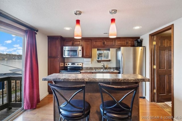 kitchen featuring sink, stainless steel appliances, decorative light fixtures, and light hardwood / wood-style floors