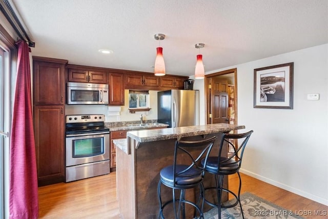 kitchen featuring appliances with stainless steel finishes, decorative light fixtures, a breakfast bar, and light hardwood / wood-style floors