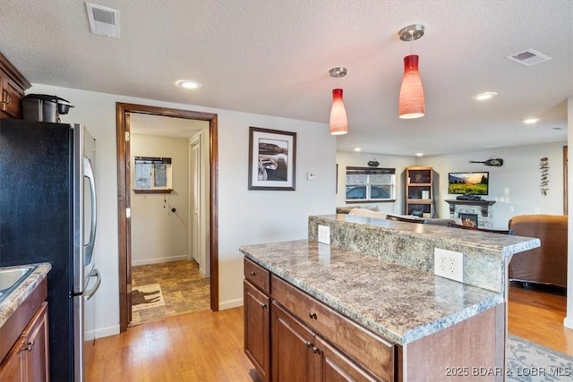 kitchen with decorative light fixtures, a textured ceiling, stainless steel refrigerator, a kitchen island, and light hardwood / wood-style floors