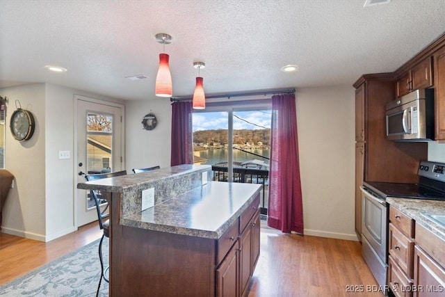 kitchen featuring a kitchen bar, a center island, hanging light fixtures, light hardwood / wood-style flooring, and stainless steel appliances