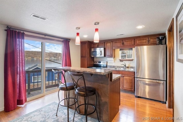 kitchen with sink, appliances with stainless steel finishes, pendant lighting, light stone countertops, and light hardwood / wood-style floors