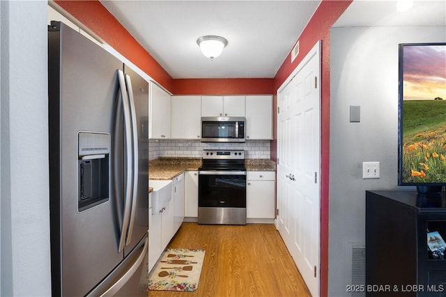 kitchen featuring light hardwood / wood-style flooring, white cabinetry, stainless steel appliances, decorative backsplash, and dark stone counters