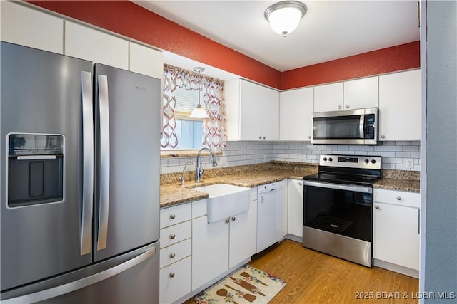 kitchen featuring appliances with stainless steel finishes, sink, white cabinets, decorative backsplash, and light hardwood / wood-style flooring