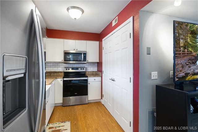 kitchen featuring white cabinetry, tasteful backsplash, dark stone countertops, light wood-type flooring, and stainless steel appliances