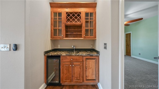 bar featuring dark stone countertops, sink, beverage cooler, and dark colored carpet