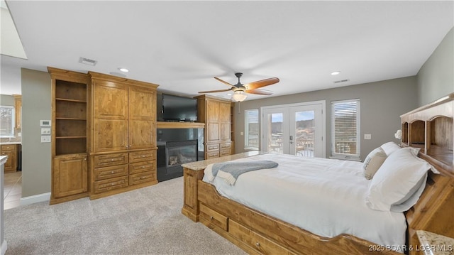 bedroom with a large fireplace, light colored carpet, access to exterior, ceiling fan, and french doors