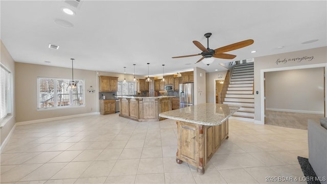 kitchen with appliances with stainless steel finishes, light stone counters, a kitchen island, decorative light fixtures, and light tile patterned flooring