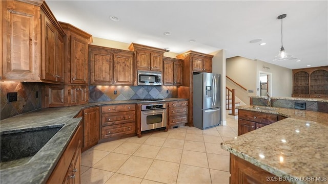 kitchen featuring light tile patterned flooring, sink, decorative light fixtures, appliances with stainless steel finishes, and dark stone counters