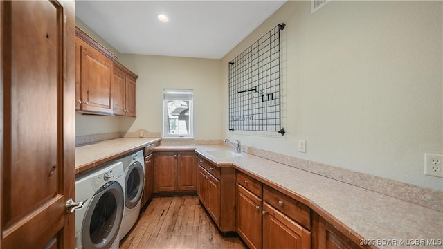 washroom with cabinets, washing machine and dryer, sink, and light hardwood / wood-style flooring