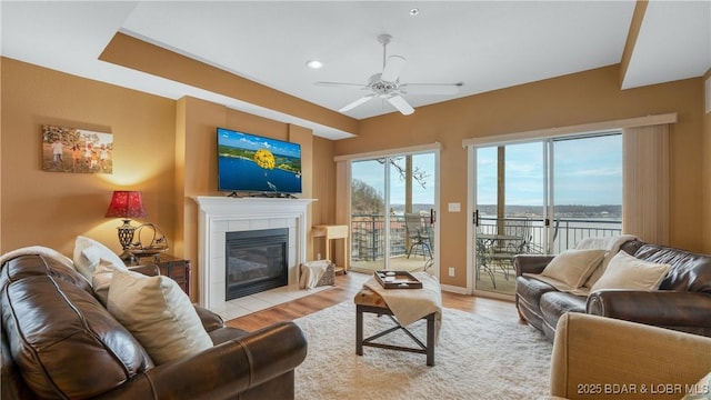 living room with a tile fireplace, ceiling fan, and light hardwood / wood-style floors