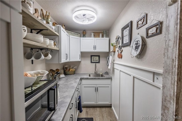 kitchen with a textured ceiling, a wainscoted wall, a sink, white cabinets, and light countertops