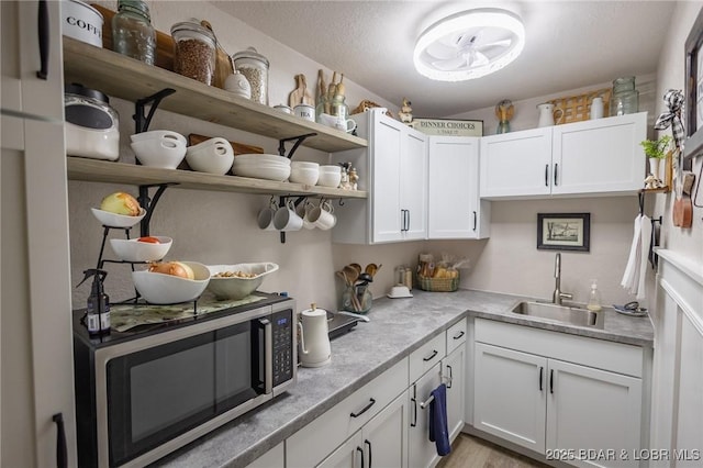 kitchen with white cabinets, stainless steel microwave, a textured ceiling, open shelves, and a sink