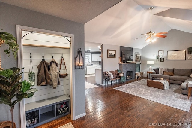 living room featuring dark wood-type flooring, lofted ceiling, a fireplace, and a ceiling fan