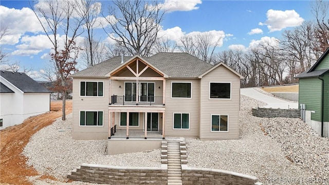 rear view of property with a balcony, covered porch, and roof with shingles