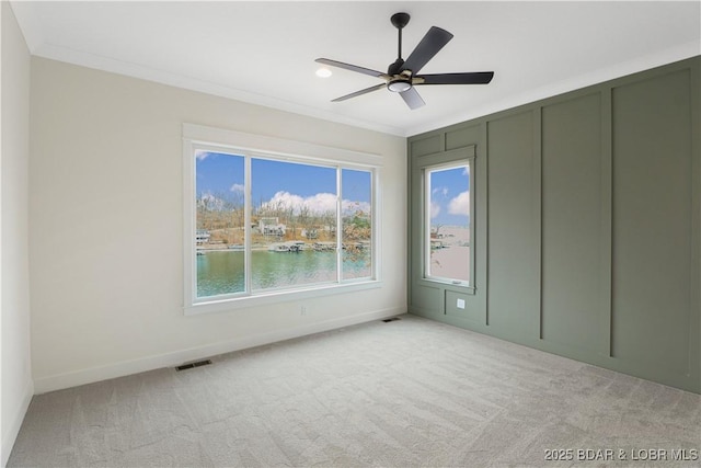 spare room with crown molding, light colored carpet, ceiling fan, and a water view