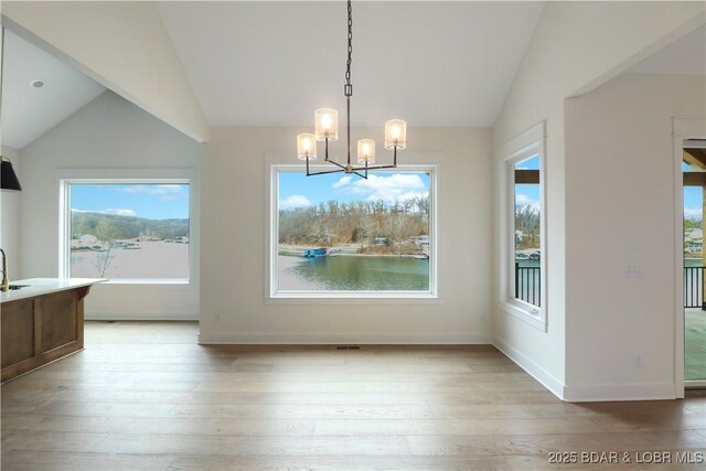 unfurnished dining area featuring a notable chandelier, vaulted ceiling, and light hardwood / wood-style floors