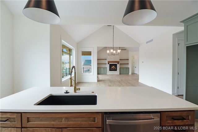 kitchen featuring lofted ceiling, sink, a large fireplace, decorative light fixtures, and stainless steel dishwasher