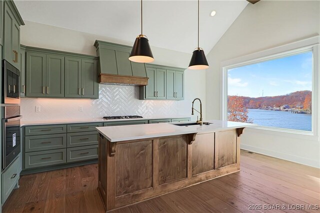 kitchen featuring sink, hanging light fixtures, stainless steel appliances, a water view, and a center island with sink