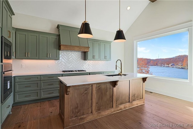 kitchen featuring stainless steel appliances, light countertops, a water view, a sink, and an island with sink