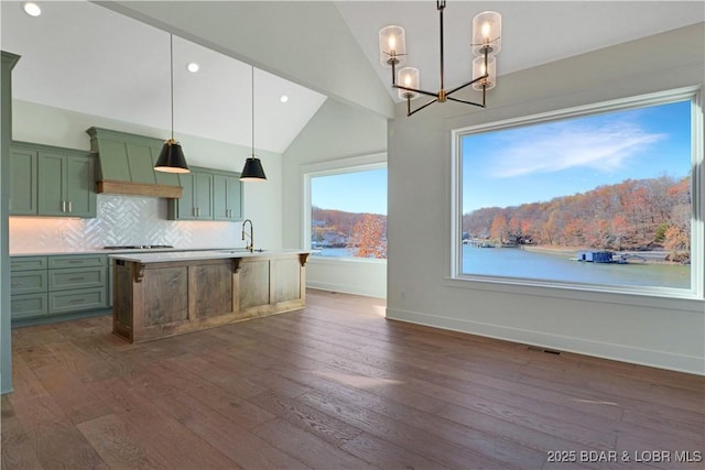 kitchen with a kitchen island with sink, hanging light fixtures, vaulted ceiling, and a water view