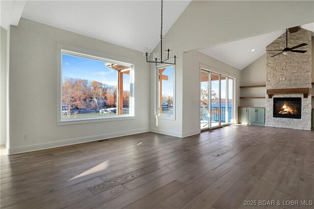 unfurnished dining area featuring a stone fireplace, ceiling fan with notable chandelier, high vaulted ceiling, and dark hardwood / wood-style floors