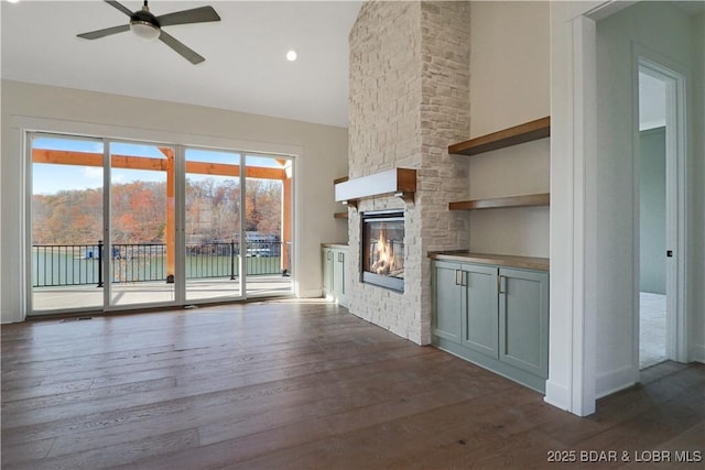 unfurnished living room with ceiling fan, a stone fireplace, dark wood-type flooring, and high vaulted ceiling