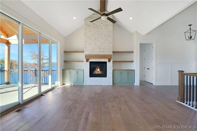 unfurnished living room featuring beam ceiling, wood-type flooring, high vaulted ceiling, ceiling fan, and a fireplace